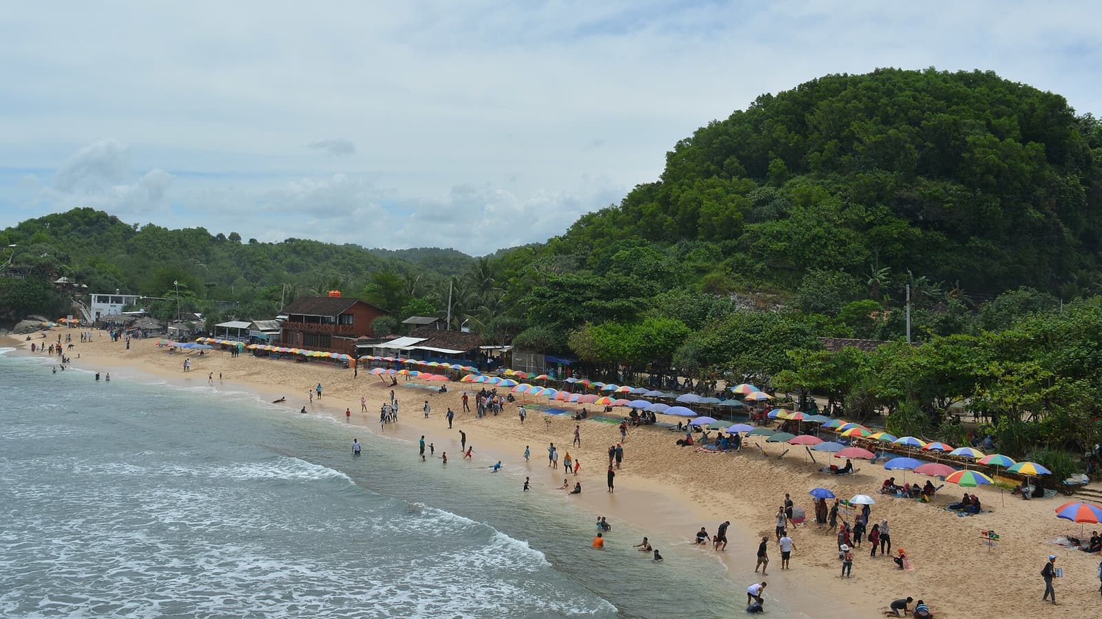 The sandy bay, beach umbrellas and green headland at Indrayanti Beach, Gunungkidul