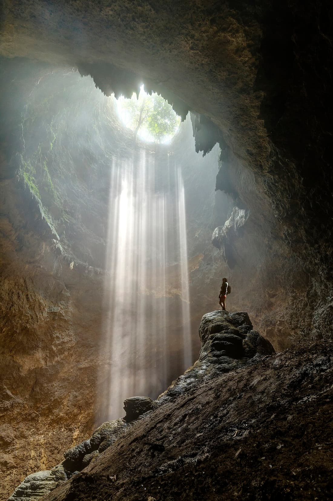 A column of sunlight falling down the shaft of Grubug Cave onto a visitor on the rocks