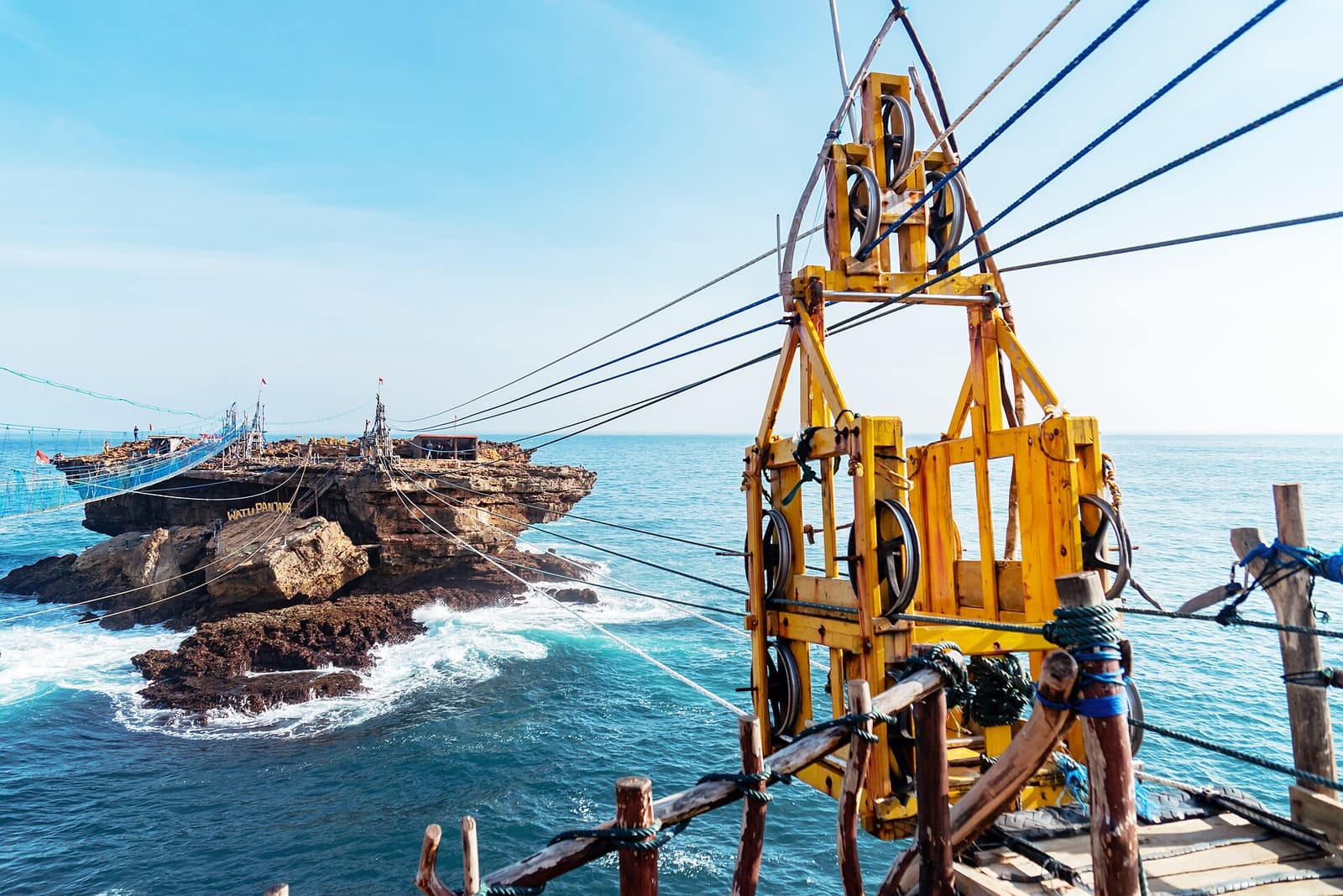 The gondola frame and ropes above the sea, with the rock island beyond, at Timang Beach