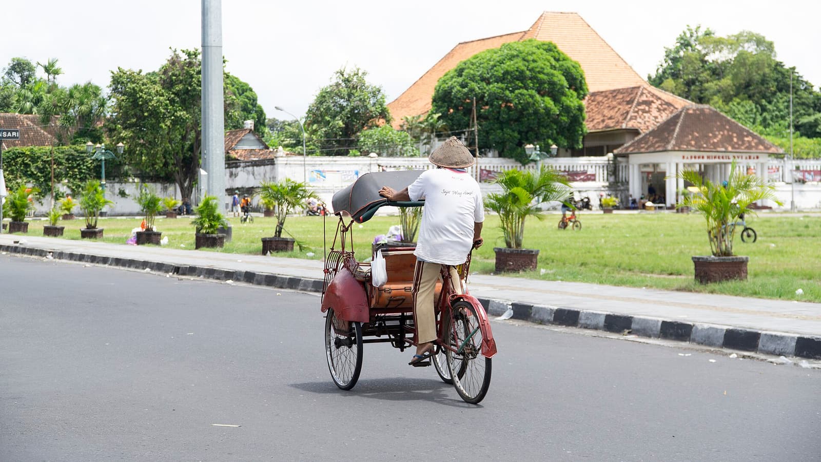 A becak pedicab driver riding along a street in Yogyakarta