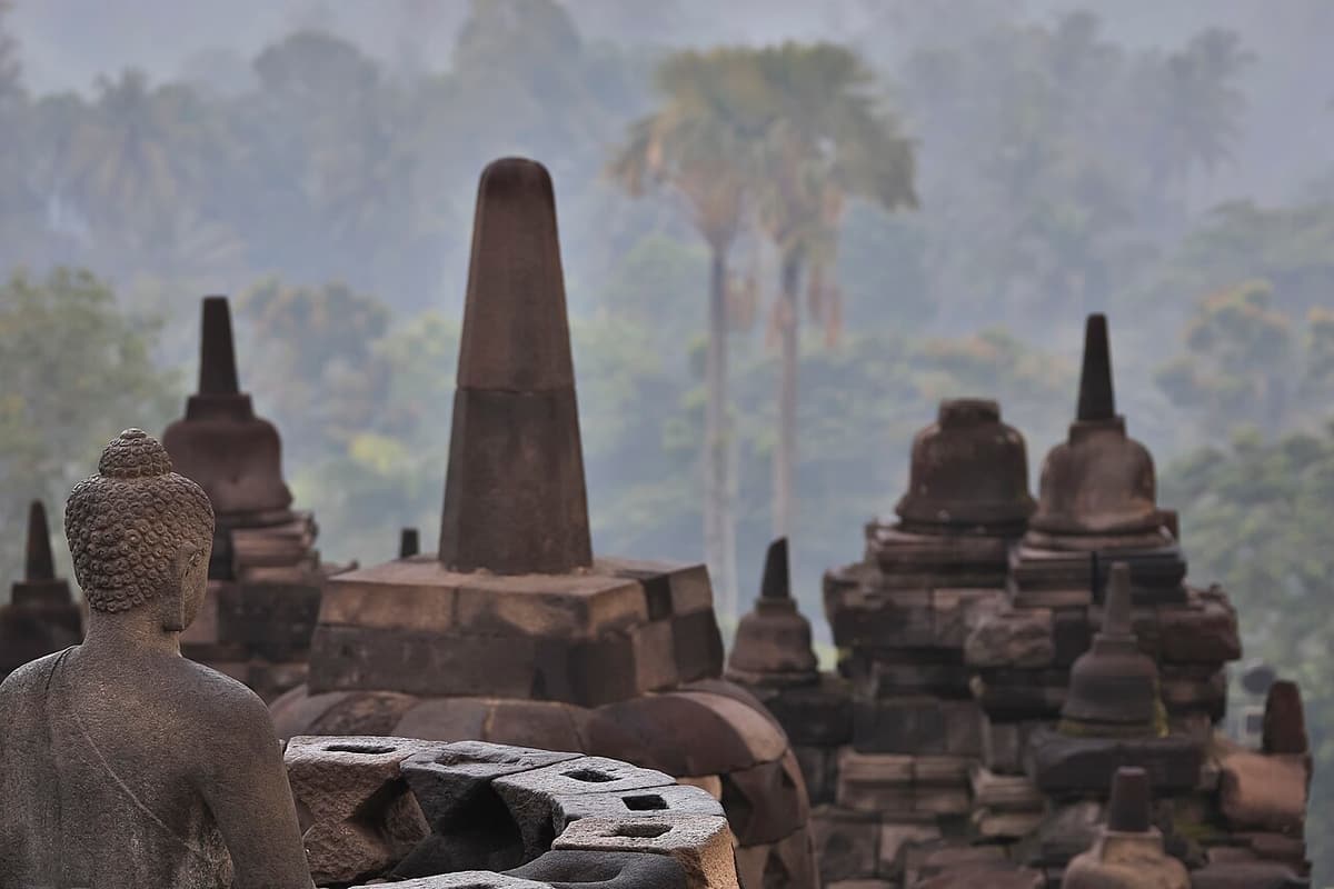 A seated Buddha statue among the stupas of Borobudur in morning mist