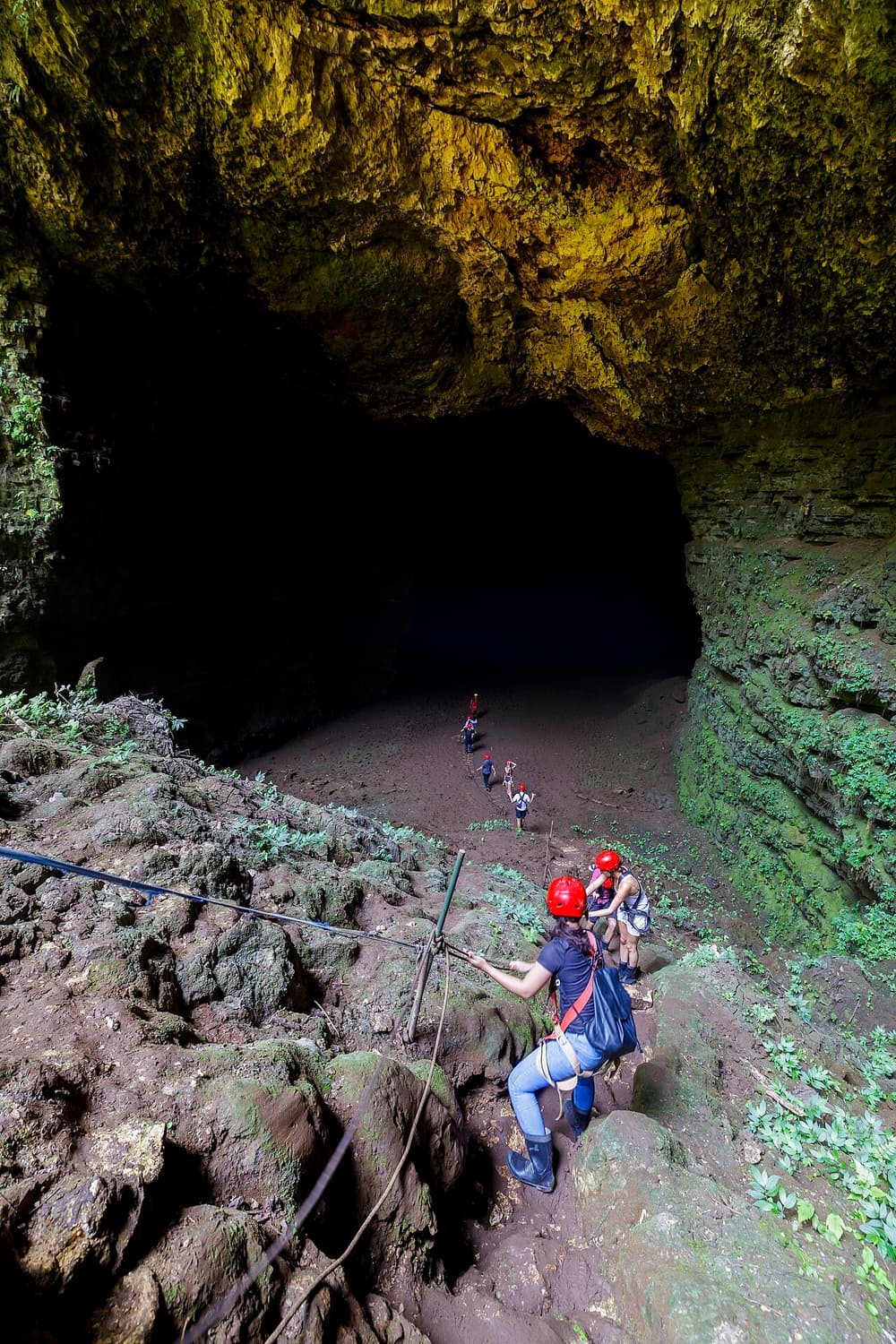 A visitor in helmet and harness on the rope beside the limestone wall of Jomblang Cave