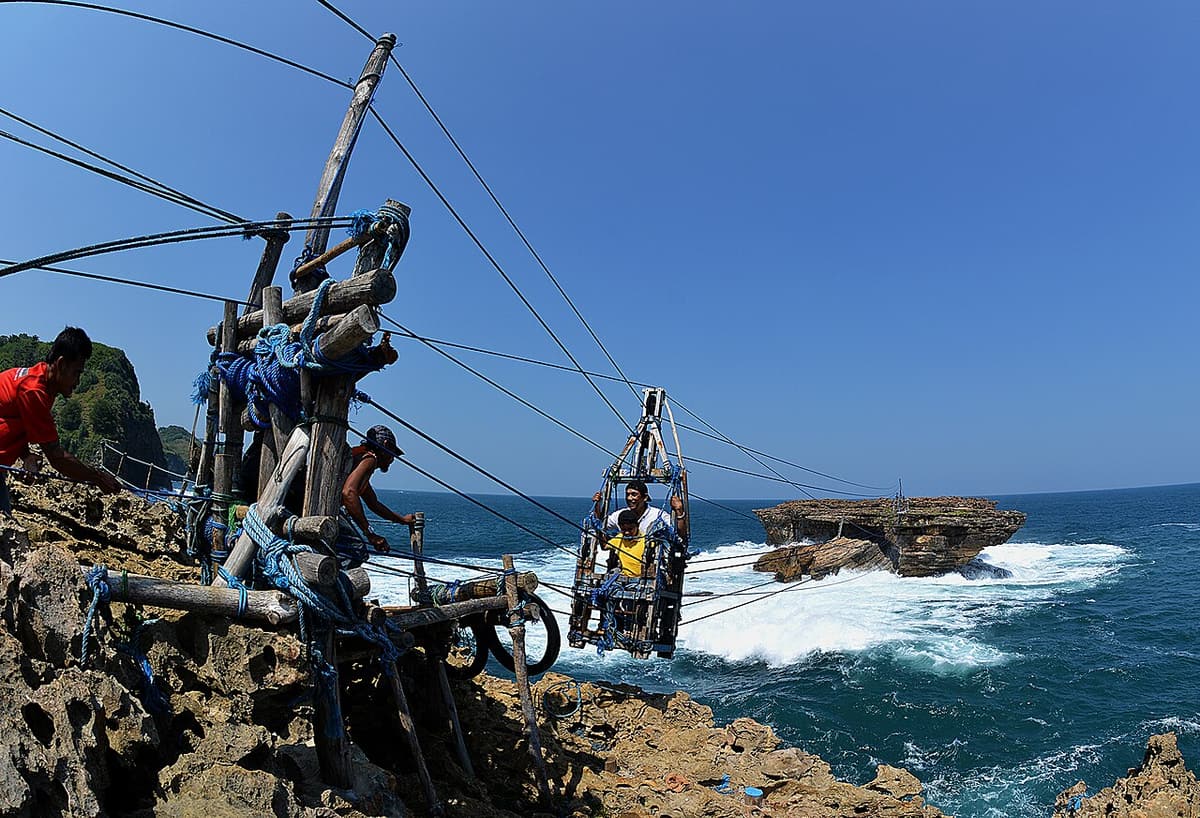 A passenger in the hand-pulled gondola above the surf at Timang Beach, with the rope crew on the cliff