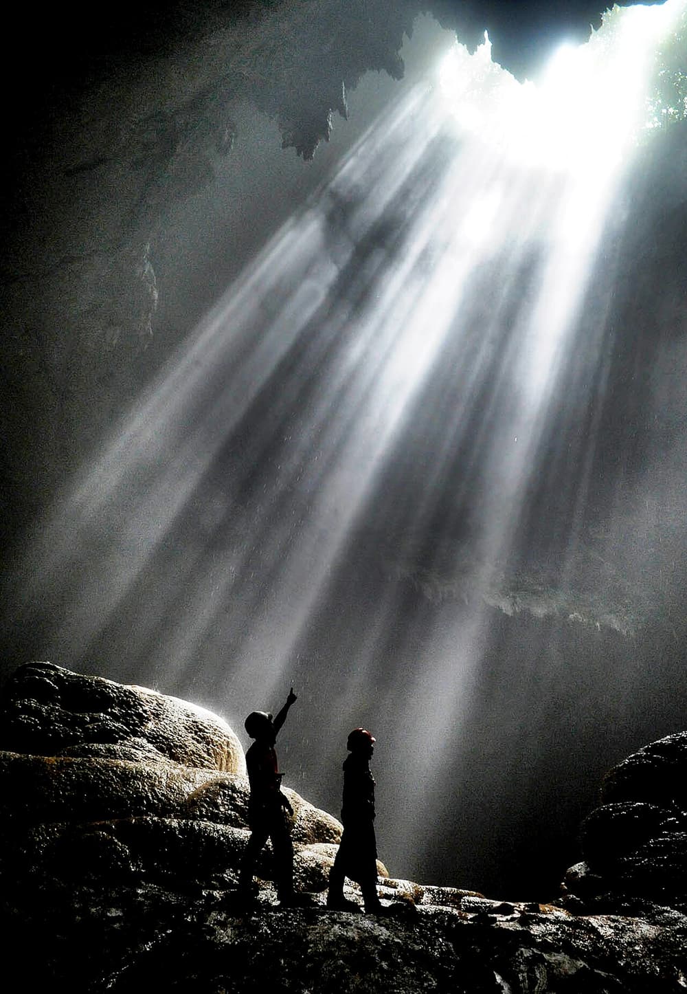 Two visitors silhouetted beneath rays of sunlight in Grubug Cave